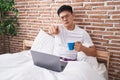 Young asian man drinking coffee sitting on the bed pointing with finger to the camera and to you, confident gesture looking Royalty Free Stock Photo