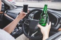 Young asian man drives a car with drunk a bottle of beer and using smartphone behind the wheel of a car