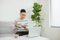 Young Asian man eating cake when sitting on sofa and using laptop Royalty Free Stock Photo