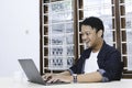 Young Asian man feeling happy and smile when work laptop on table. Indonesian man wearing blue shirt Royalty Free Stock Photo