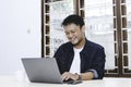 Young Asian man feeling happy and smile when work laptop on table. Indonesian man wearing blue shirt