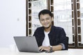 Young Asian man feeling happy and smile when work laptop on table. Indonesian man wearing blue shirt