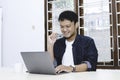 Young Asian man feeling happy and smile when work laptop on table. Indonesian man wearing blue shirt