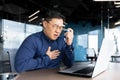 Young Asian man having asthma attack, panic attack, pneumonia at workplace, holding an inhaler Royalty Free Stock Photo