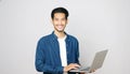 Young asian man holding laptop computer smiling and looking at camera standing on isolated grey background, people and technology Royalty Free Stock Photo