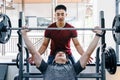 Young Asian man lifting heavy weight working on his upper body workout with his male trainer at a gym