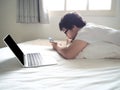 Young Asian man with mobile smart phone lying down on the bed in morning. Internet of things concept Royalty Free Stock Photo