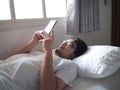 Young Asian man with mobile smart phone lying down on the bed Royalty Free Stock Photo