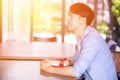 Young Asian man patiently sitting in cafe restaurant and holding a present gift giving to someone special for special occasion. Royalty Free Stock Photo