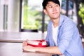 Young Asian man patiently sitting in cafe restaurant and holding a present gift giving to someone special for special occasion. Royalty Free Stock Photo