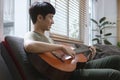 Young asian man playing guitar while sitting on sofa at home Royalty Free Stock Photo