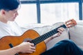 Young asian man playing guitar while sitting on sofa in living room Music is his life He love playing guitar Composing and Royalty Free Stock Photo