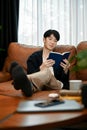 Young Asian man reading book relaxing on his sofa during the weekend Royalty Free Stock Photo
