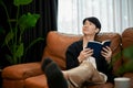 Young Asian man reading book relaxing on his sofa during the weekend Royalty Free Stock Photo