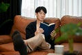 Young Asian man reading book relaxing on his sofa Royalty Free Stock Photo