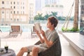 A young asian man is relaxing near the outdoor pool with a book in his hands Royalty Free Stock Photo