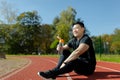 Young Asian man resting after jogging, competition, sitting on treadmill in stadium and drinking water from bottle Royalty Free Stock Photo