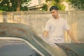 Young Asian man with rusty old car in the streets outdoors