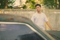 Young Asian man with rusty old car in the streets outdoors