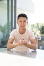 Young Asian man sits at a table, smiling confidently on a video call