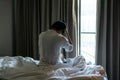 Young Asian man sitting alone on bed at home felling sad, depresses or worry and hiding his face behind hand. Unhappy and stress