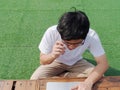 Young Asian man sitting on grass and working on computer laptop. Royalty Free Stock Photo