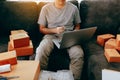 Young asian man sitting on sofa looking on computer laptop and writing order list on paper, SME concept Royalty Free Stock Photo