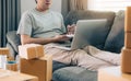 Young asian man sitting on sofa looking on computer laptop and writing order list on paper, SME concept Royalty Free Stock Photo