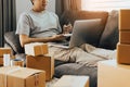 Young asian man sitting on sofa looking on computer laptop and writing order list on paper, SME concept Royalty Free Stock Photo