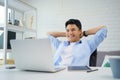 Young Asian man is smiling and reading the screen on laptop while relaxing and working at home