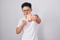 Young asian man standing over white background punching fist to fight, aggressive and angry attack, threat and violence Royalty Free Stock Photo