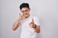 Young asian man standing over white background smiling doing talking on the telephone gesture and pointing to you Royalty Free Stock Photo