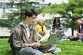 Young asian man student using laptop on green grass in front of university building. Education, technology and lifestyle