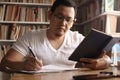 Young Asian man studying in library, exam preparation concept. Male college student doing research and making notes in his book Royalty Free Stock Photo