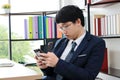 Young Asian man in suit looking mobile smart phone in hands in office Royalty Free Stock Photo