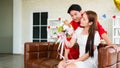 A young Asian man surprised his girlfriend by giving her a rose and flower bouquet for her anniversary date at home. Asian woman Royalty Free Stock Photo