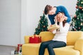 Young Asian man surprises and closes her eyes with a Christmas gift at home with a Christmas tree in the background.