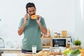 Young Asian man talking on phone in apartment in kitchen in morning after waking up, Wear comfortable pajamas, reaching out pick Royalty Free Stock Photo