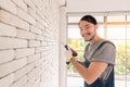 Young Asian man using electric drill on white brick wall in room