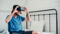 Young Asian man using glasses virtual reality simulator playing video game in bedroom, Japanese male feeling happy using relax Royalty Free Stock Photo