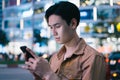 Young asian man is using his phone while walking in the street at night Royalty Free Stock Photo