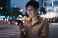 Young asian man is using his phone while walking in the street at night Royalty Free Stock Photo