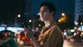 Young asian man is using his phone while walking in the street at night Royalty Free Stock Photo