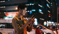 Young asian man is using his phone while walking in the street at night Royalty Free Stock Photo