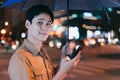 Young asian man is using his phone while walking in the street at night Royalty Free Stock Photo