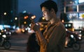 Young asian man is using his phone while walking in the street at night Royalty Free Stock Photo