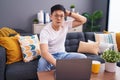 Young asian man using laptop at home sitting on the sofa crazy and scared with hands on head, afraid and surprised of shock with Royalty Free Stock Photo