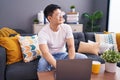 Young asian man using laptop at home sitting on the sofa looking away to side with smile on face, natural expression Royalty Free Stock Photo