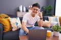 Young asian man using laptop at home sitting on the sofa smiling doing phone gesture with hand and fingers like talking on the Royalty Free Stock Photo