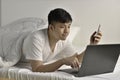 Young Asian man using laptop and smartphone in bed after waking up in the morning Royalty Free Stock Photo